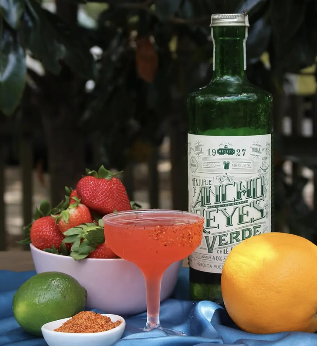 Girl Is A Gun cocktail presented with strawberries, citrus, and Ancho Reyes Verde